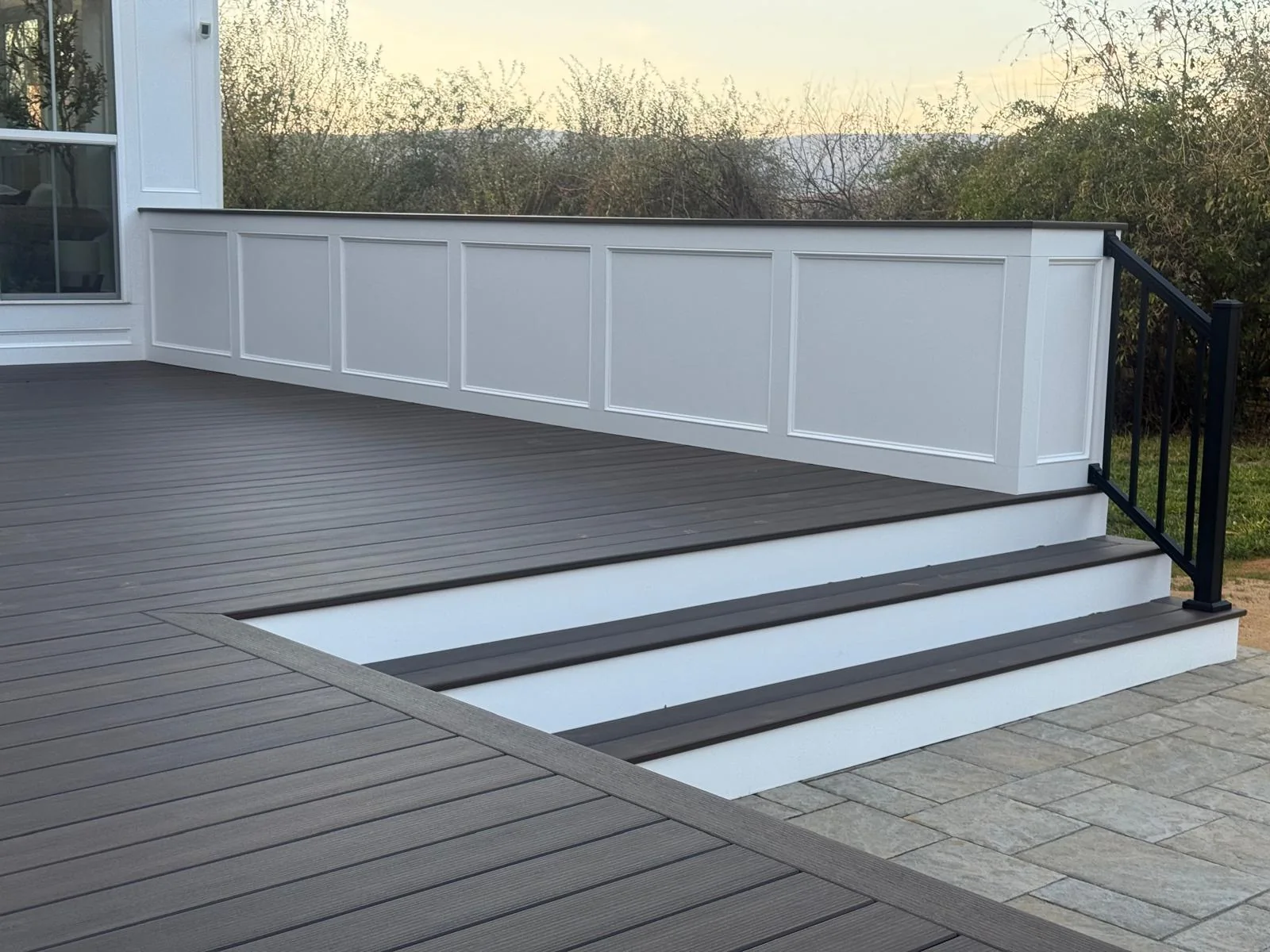 Dark deck stair treads with white risers beside a paneled privacy wall and black railing in Leesburg